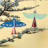 Two colorful cardboard bird ornaments hanging from a pine tree branch against a soft yellow background.