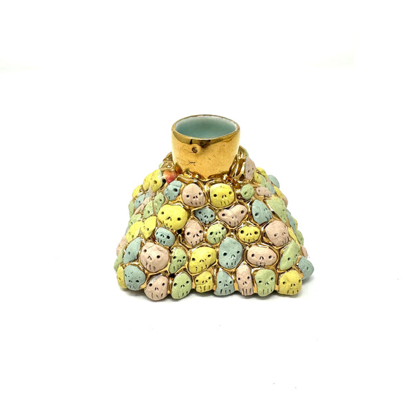 Decorative candle holder with pastel-colored skull faces on a white background