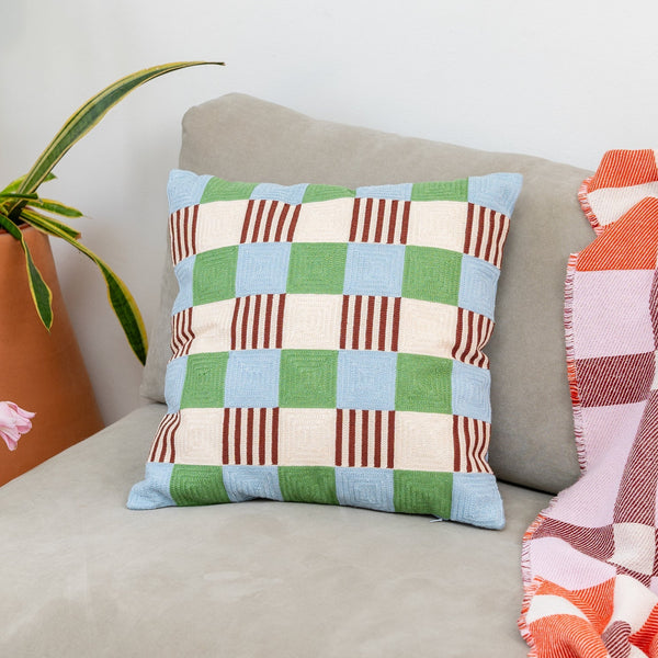 Checkered pillow on a couch with a plant and blanket in the background