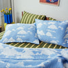 Blue cloud-patterned pillows and blanket on a bed with a striped headboard, yellow flowers, and a poster in the background.