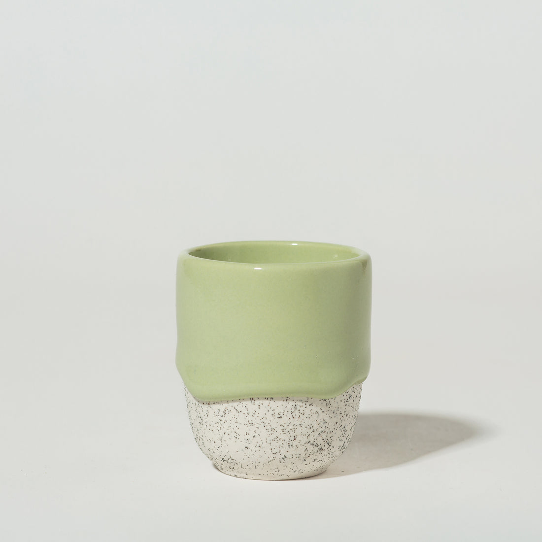 A green ceramic espresso cup with a speckled white bottom.