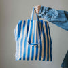 Person holding a blue and white striped tote bag against a plain background