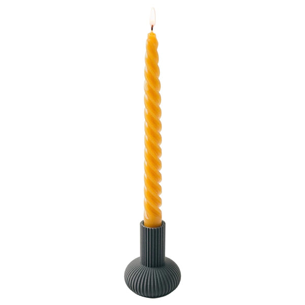 Yellow twisted candle on a black holder against a white background